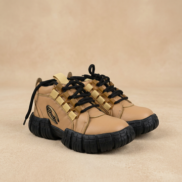 Tan boys shoes with black laces and soles on a light beige background