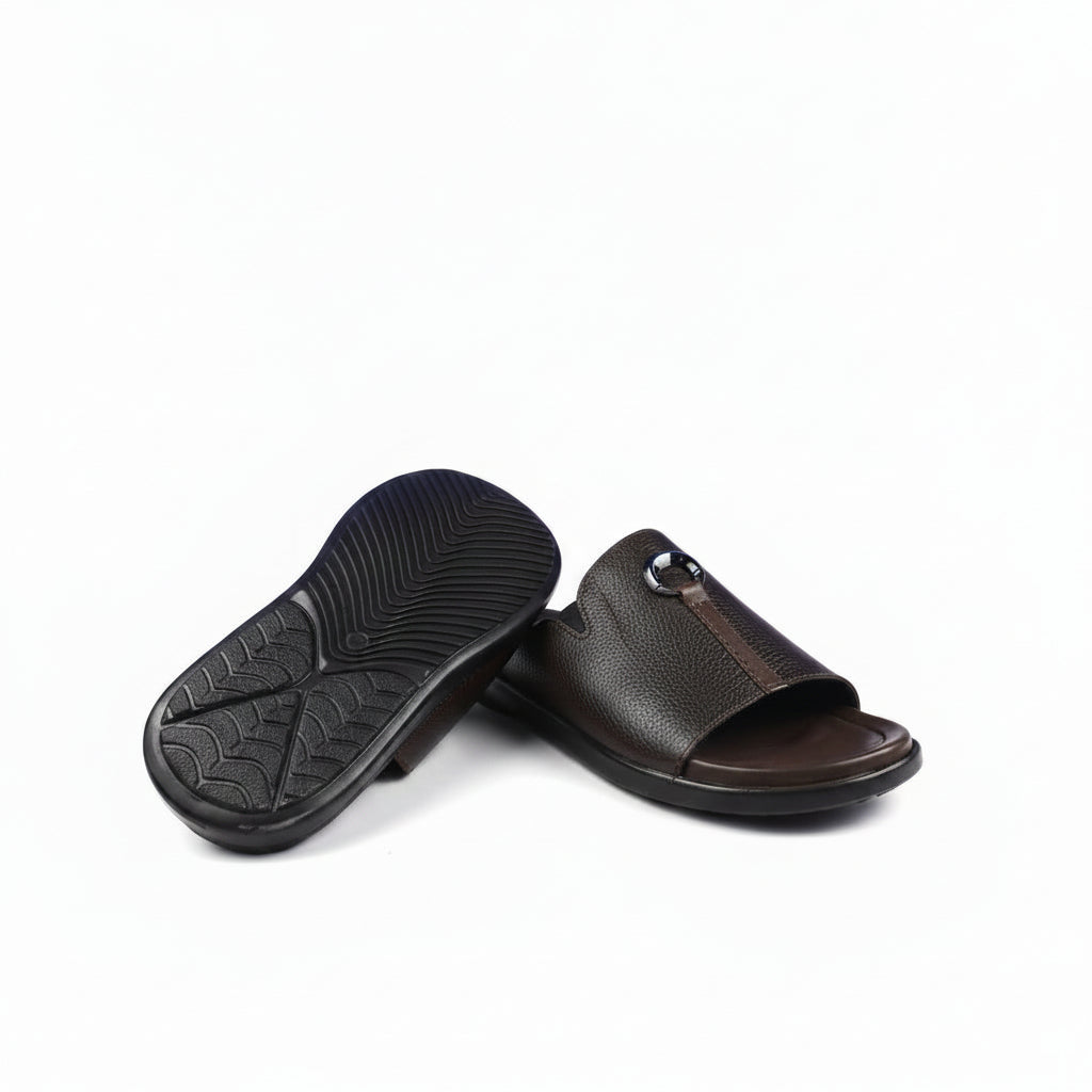 A pair of black pebbled leather slide sandals with a circular metal ring detail on the strap, shown on a clean white background.