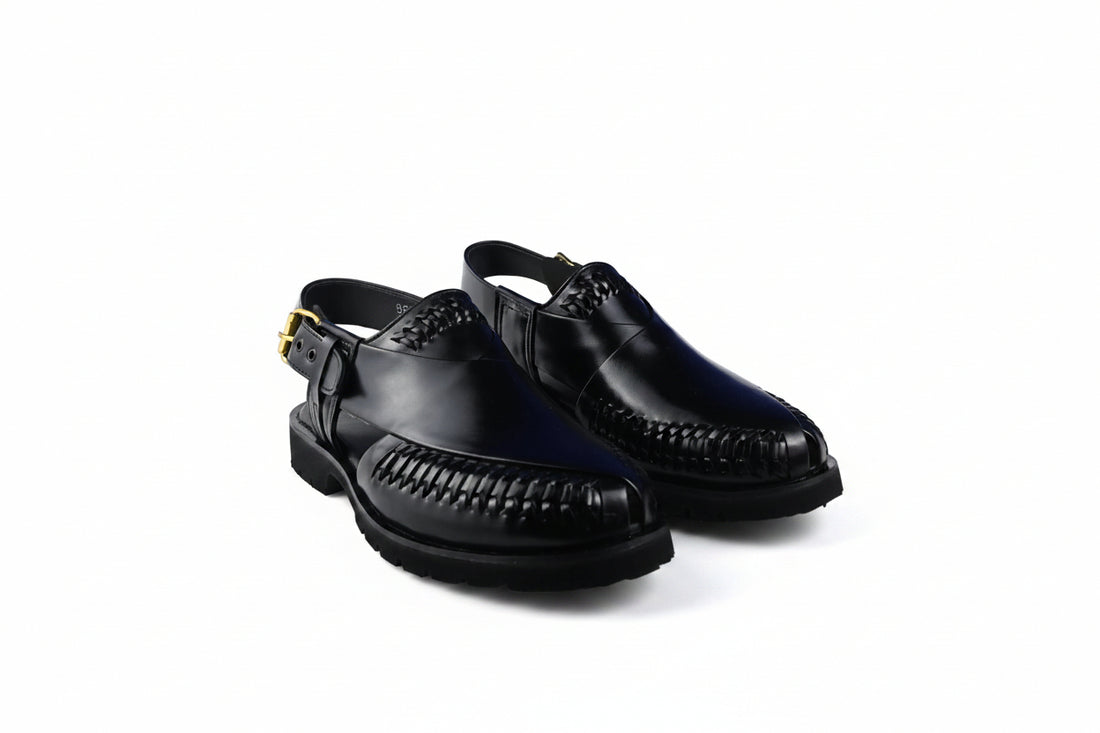 A pair of black  slingback moccasin-style shoes with braided detailing on the toe and a small gold buckle, shown on a plain white background.