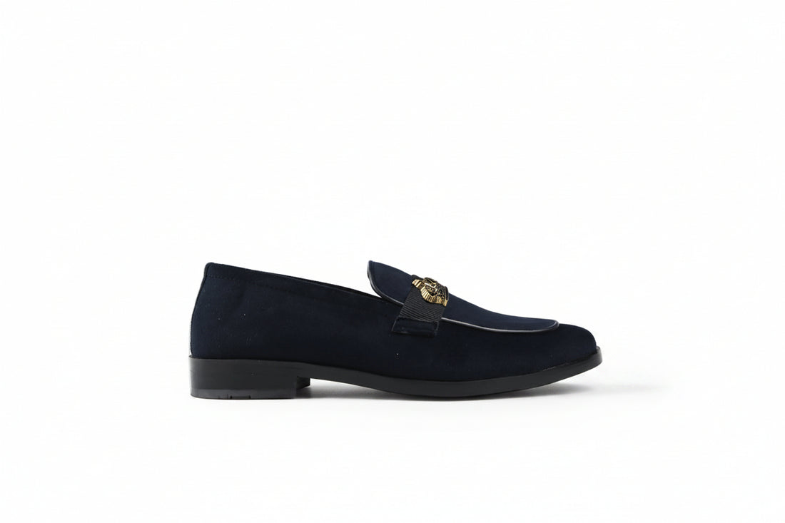 A pair of dark navy blue velvet loafers with a black strap across the vamp featuring a gold-tone crown emblem, set against a plain white background.