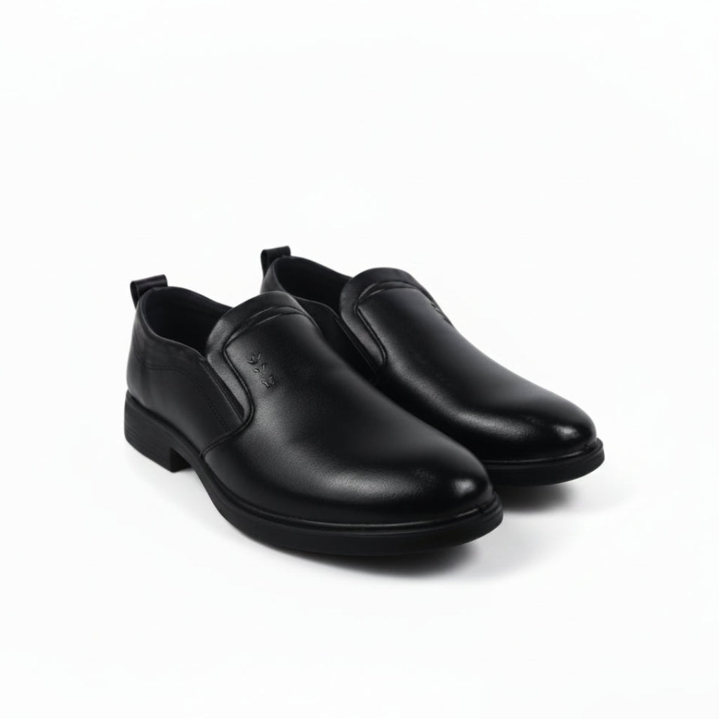 A pair of black  slip-on loafers with low block heels, displayed on a light gray background with a small tag attached to a black cord in the lower left corner.