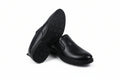 A pair of black  slip-on shoes, with one shoe standing upright to show the textured outsole and the other lying on its side to show the side profile, set against a plain white background.
