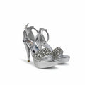 A pair of metallic silver high-heeled sandals with platform soles and sparkling rhinestone embellishments on the straps, set against a plain light gray background.