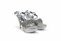 A pair of metallic silver high-heeled sandals with crystal-embellished straps and glittery platform soles, photographed on a light gray studio background.