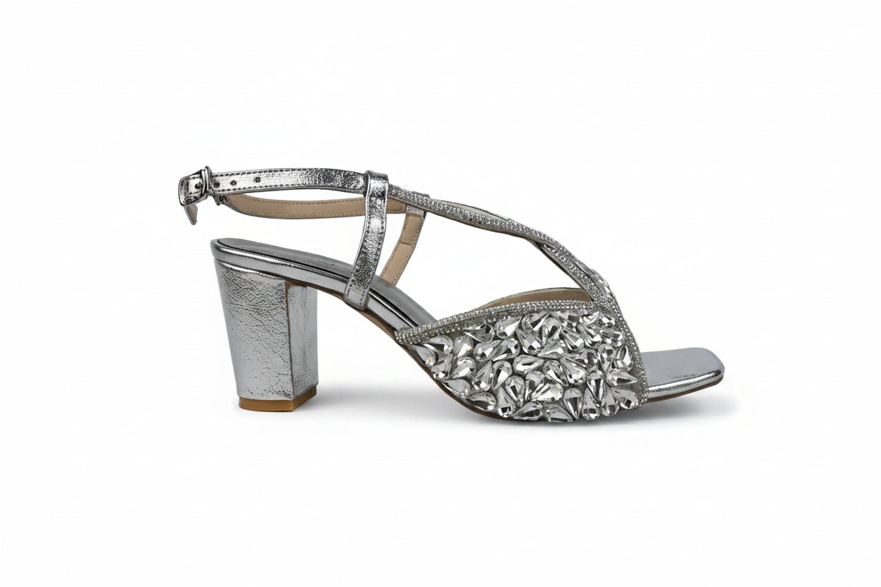 A single silver metallic block-heel sandal with an ankle strap and a wide front strap heavily embellished with silver rhinestones, shown against a light gray background.