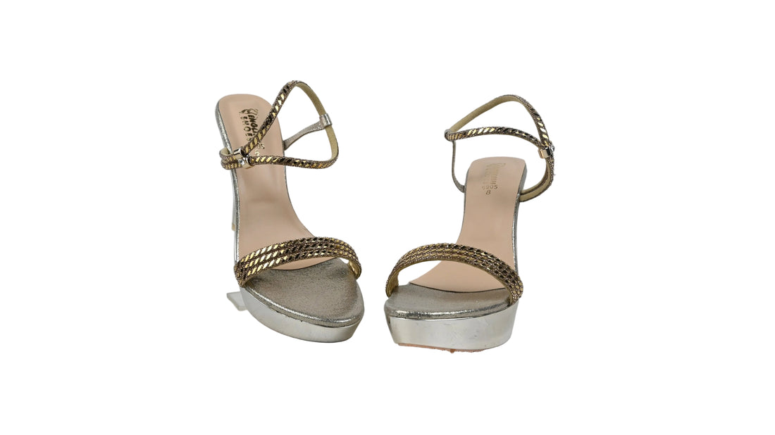 A pair of metallic silver high-heeled sandals with platform soles and braided strap details, photographed against a light gray textured background.