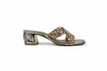 A single women's heeled mule sandal with a gold-tone metallic frame, a chunky block heel featuring a black and white geometric pattern, and a wide crisscross front strap embellished with gold rhinestones, shown against a light gray background.