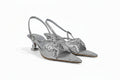A pair of metallic silver slingback kitten heel sandals with pointed toes and large bow embellishments on the front, displayed against a light gray background.