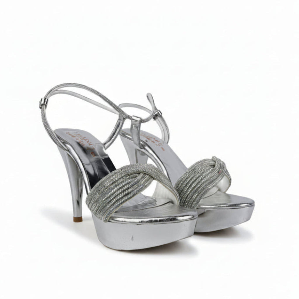 A pair of silver metallic high-heeled sandals with platform soles and rhinestone-embellished straps, shown against a wrinkled light gray background.