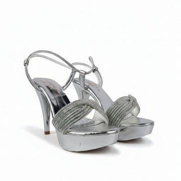 A pair of silver metallic high-heeled sandals with platform soles and rhinestone-embellished straps, shown against a wrinkled light gray background.