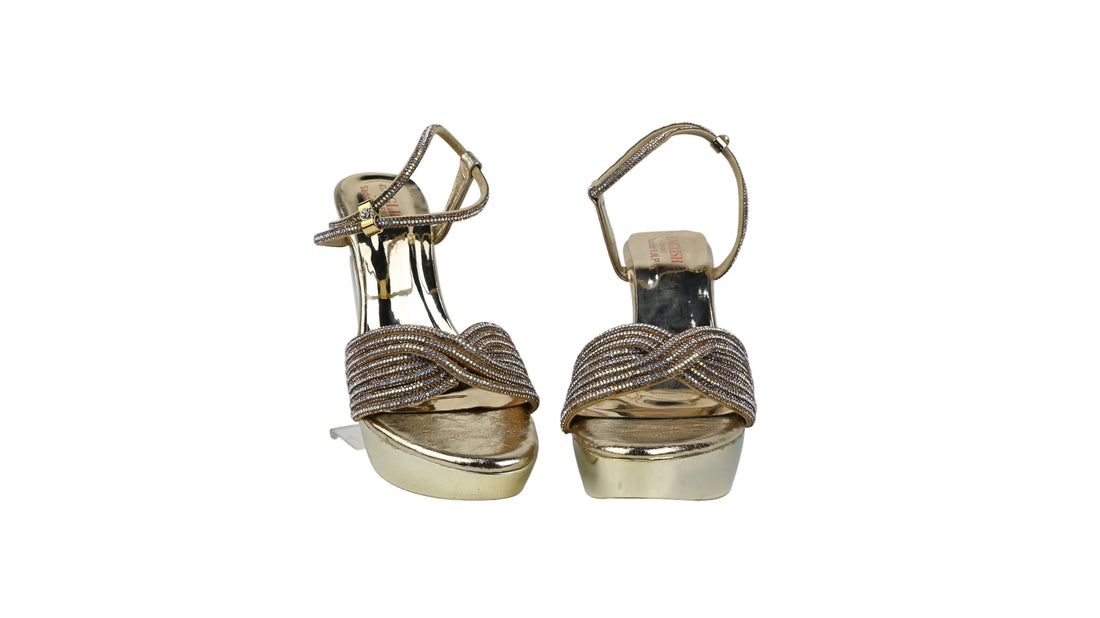 A pair of silver metallic high-heeled sandals with platform soles and rhinestone-embellished straps, shown against a wrinkled light gray background.