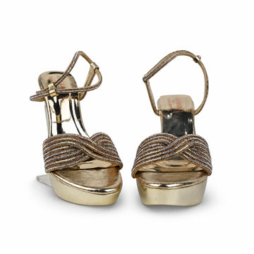 A pair of metallic gold platform sandals with criss-cross metallic straps, photographed against a light gray fabric backdrop.