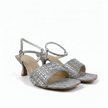 A pair of women's silver heeled sandals with rhinestone-embellished straps and a textured metallic upper, shown on a light gray studio background.