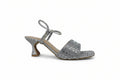 A single women's heeled sandal in metallic silver with rhinestone embellishments, a square toe, and a low kitten heel, shown against a light gray background.