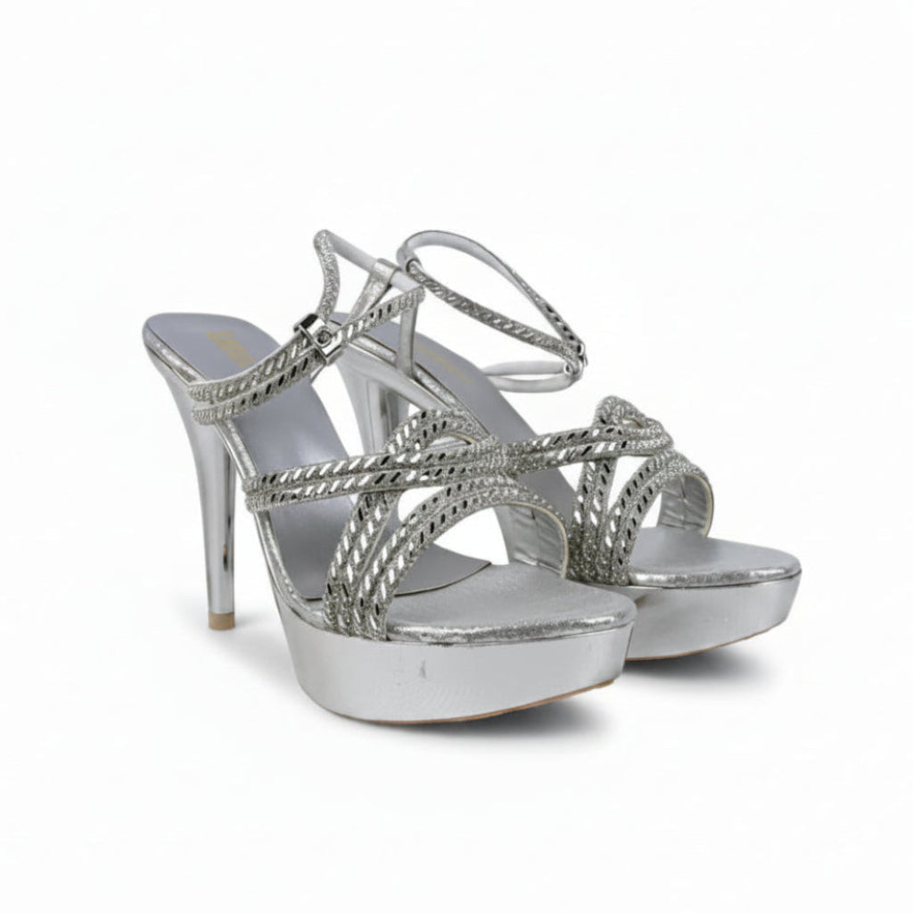 A pair of metallic silver high-heeled sandals with platform soles and crisscross ankle straps, photographed against a white studio backdrop.