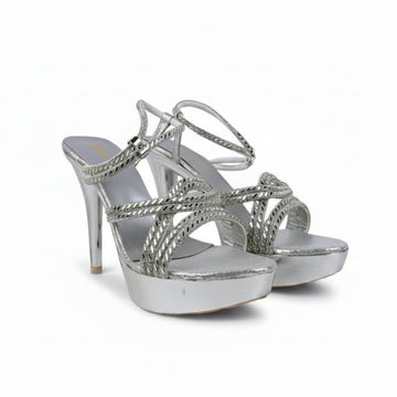 A pair of metallic silver high-heeled sandals with platform soles and crisscross ankle straps, photographed against a white studio backdrop.