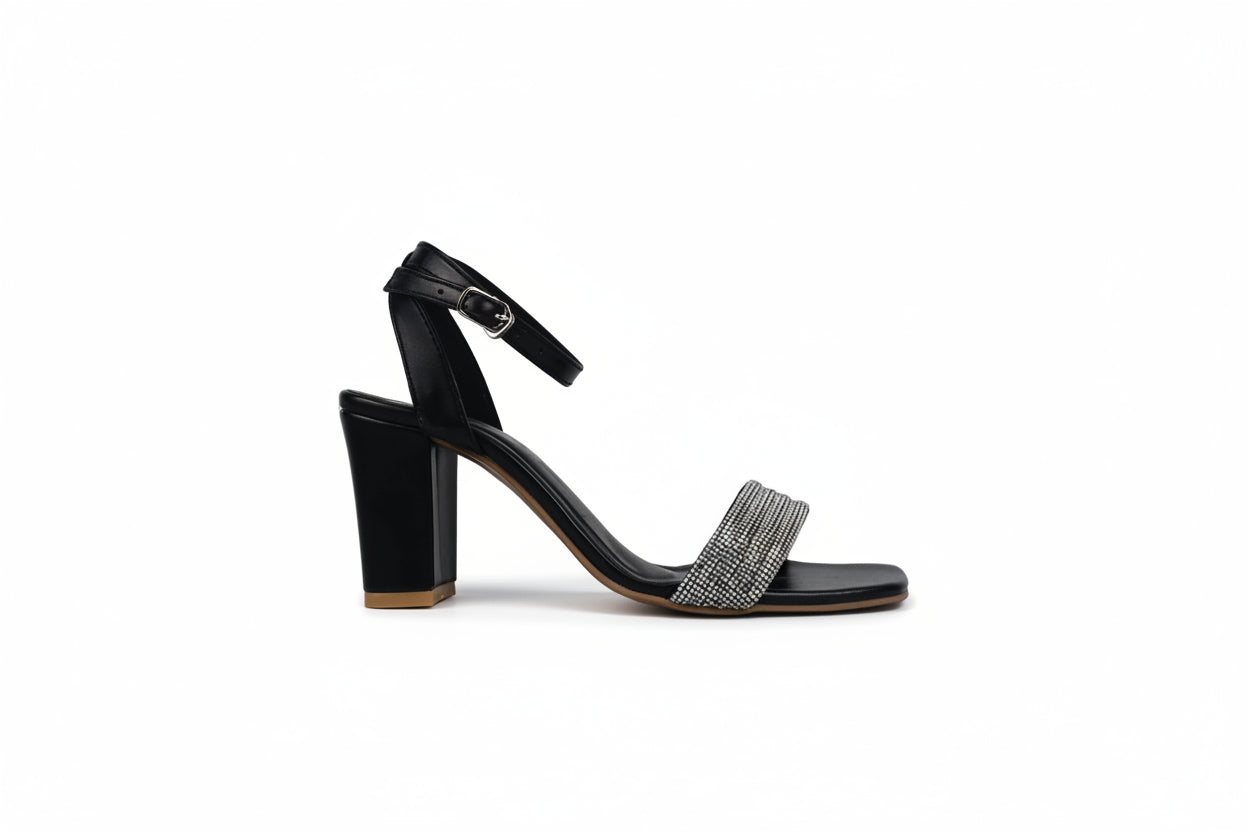 A single black high-heeled sandal with an ankle strap and a sparkling rhinestone-embellished toe strap, shown from the side against a light gray background.