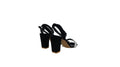 A pair of women's black high-heeled sandals with block heels and ankle straps, shown on a light gray studio background.