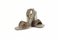 A pair of metallic gold high-heeled sandals with intricate crystal and bead embellishments on the straps, set against a plain light gray background.