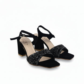 A pair of black high-heeled sandals with ankle straps and sparkling silver embellishments on the square toes, shown on a white studio background.