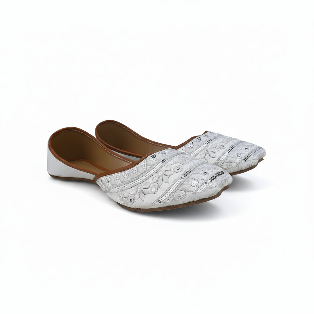 A pair of white embroidered flat shoes with brown inner soles, displayed on a light gray fabric background.