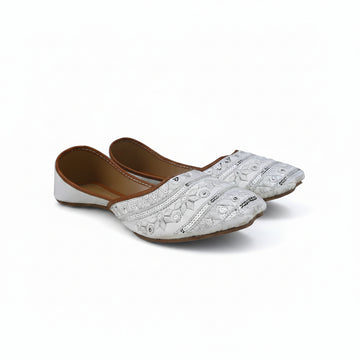 A pair of white embroidered flat shoes with brown inner soles, displayed on a light gray fabric background.