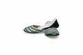 A pair of traditional flat shoes with green and white patterned uppers and solid green heels, displayed on a white surface against a white fabric backdrop.