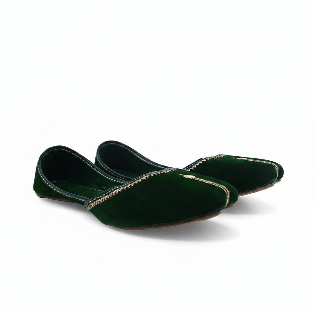 A pair of dark green velvet flat shoes with gold embroidered detailing along the toe, displayed on a light gray fabric background.