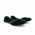 A pair of dark green velvet flat shoes with gold embroidered detailing along the toe, displayed on a light gray fabric background.