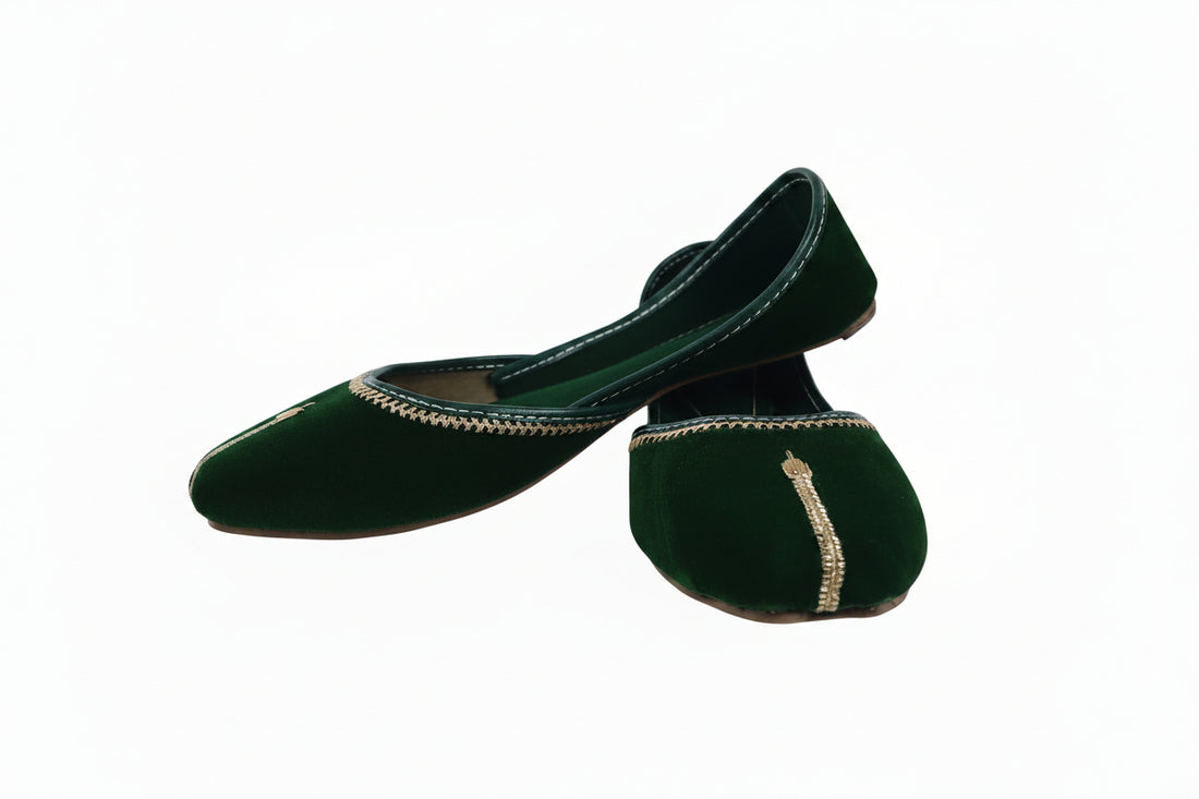 A pair of dark green velvet flat shoes with gold embroidered detailing along the toe, displayed on a light gray fabric background.