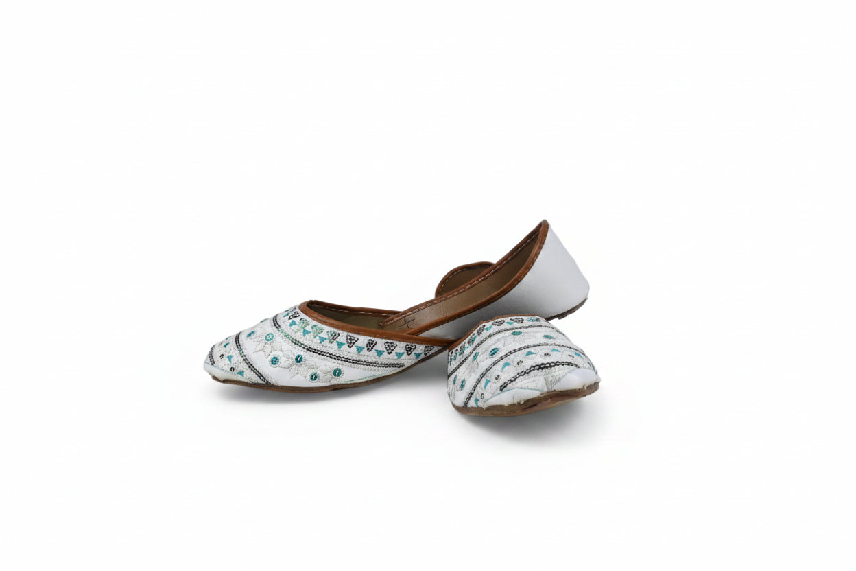 A pair of traditional white leather mule slippers with blue and black embroidered patterns, displayed against a plain light gray background.