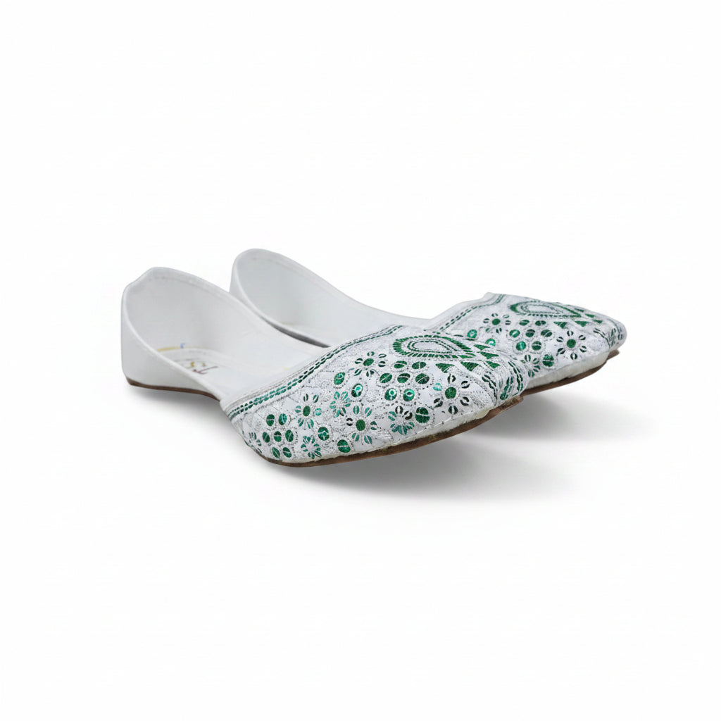A pair of white flat slip-on shoes decorated with green sequins and beadwork, displayed on a light gray surface.