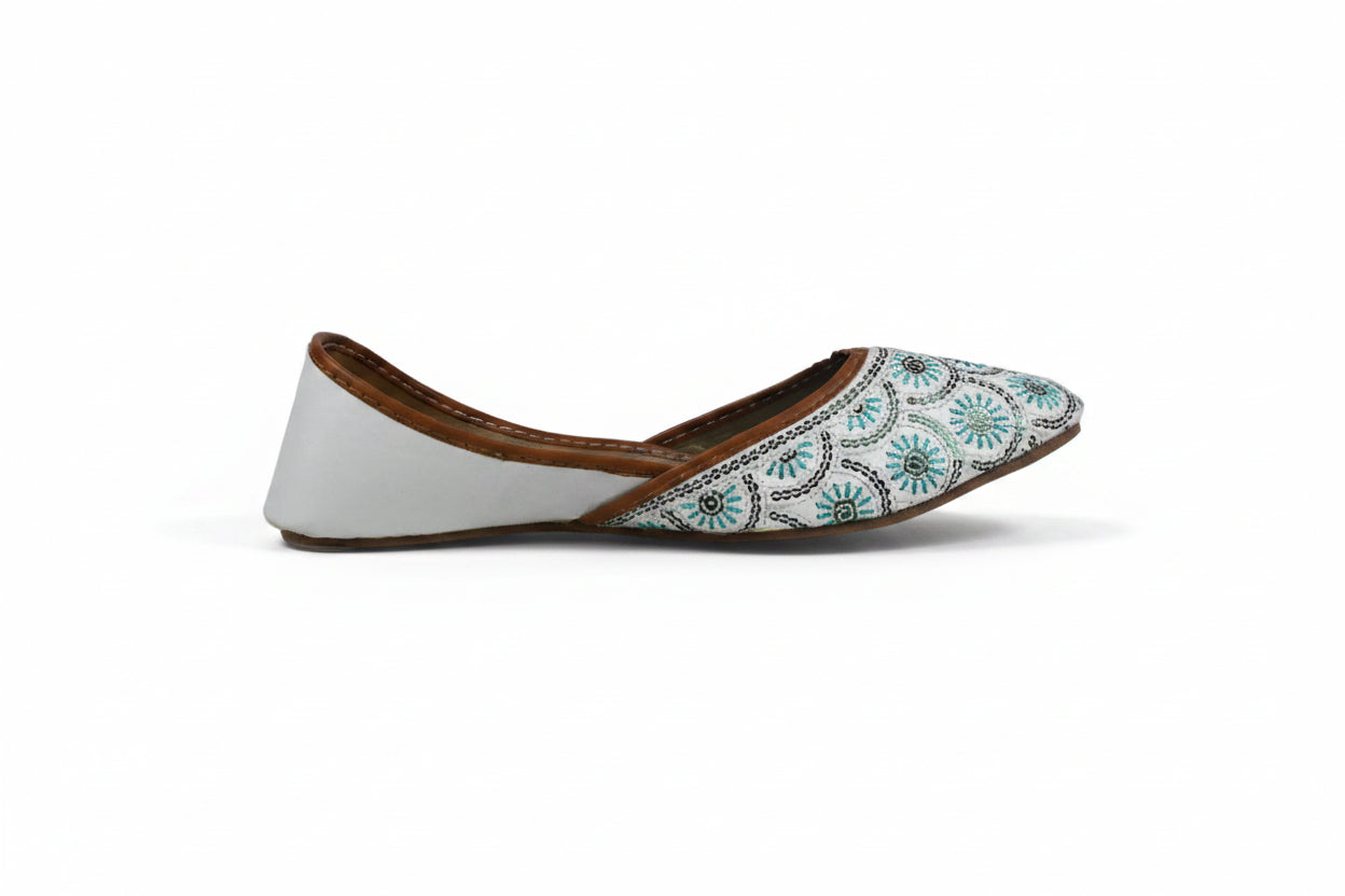 A single white flat shoe with a brown leather trim and a blue and green floral pattern on the toe cap, shown against a light gray background.
