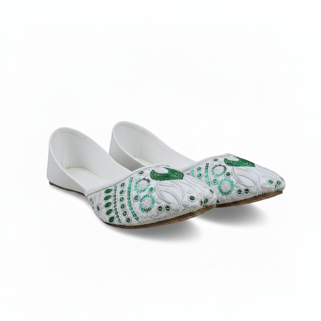 A pair of white flat shoes with intricate green and turquoise beadwork and sequins on the toe caps, photographed on a light gray surface.