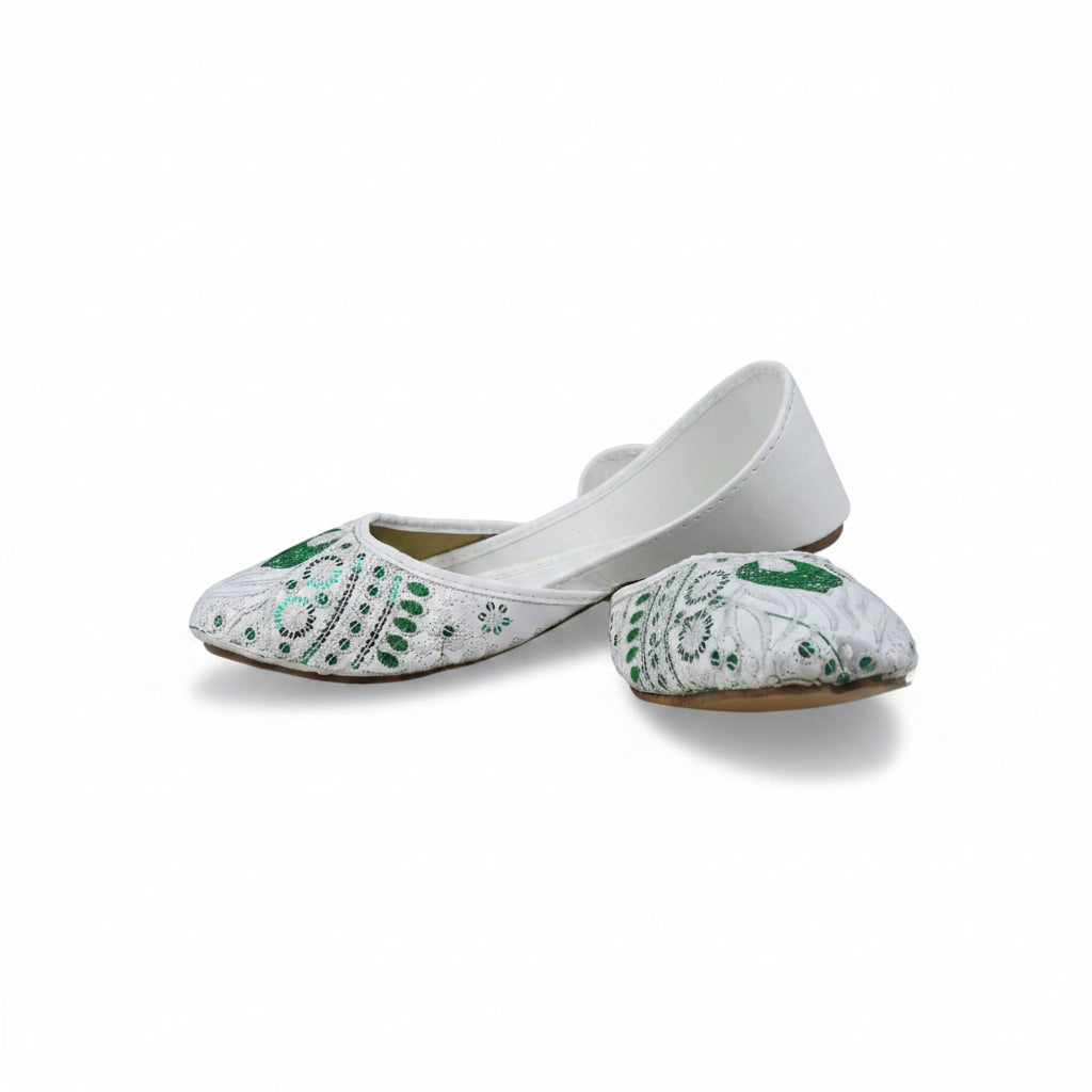 A pair of white flat shoes with intricate green and turquoise beadwork and sequins on the toe caps, photographed on a light gray surface.
