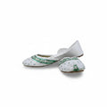 A pair of white traditional flat shoes with green embroidered detailing on the toe area, photographed against a light gray fabric backdrop.