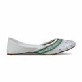 A single white flat shoe with green embroidered detailing and small rhinestone embellishments on the toe, shown against a light gray background.