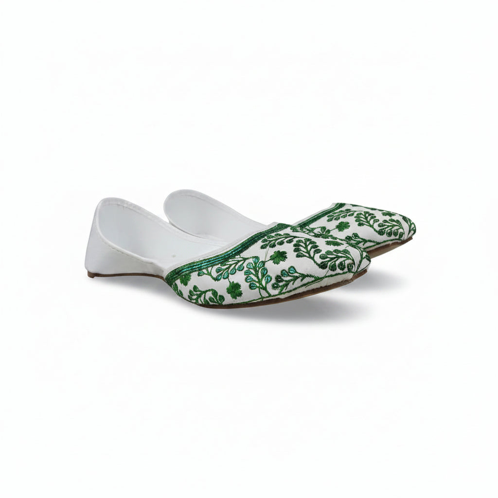 A single white slip-on flat shoe with green floral embroidery around the toe, photographed against a light gray fabric backdrop.