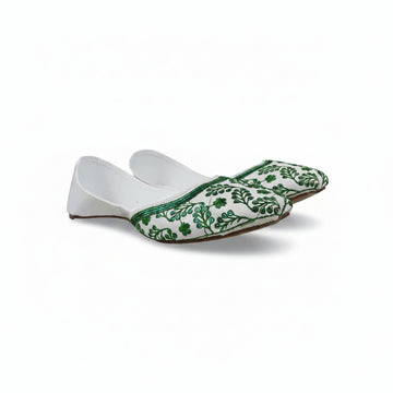 A single white slip-on flat shoe with green floral embroidery around the toe, photographed against a light gray fabric backdrop.