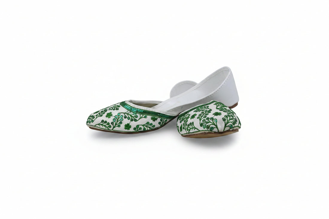 A single white slip-on flat shoe with green floral embroidery around the toe, photographed against a light gray fabric backdrop.