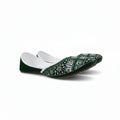 A single green velvet flat shoe with intricate white and silver embroidery on the toe, photographed on a light gray fabric background.