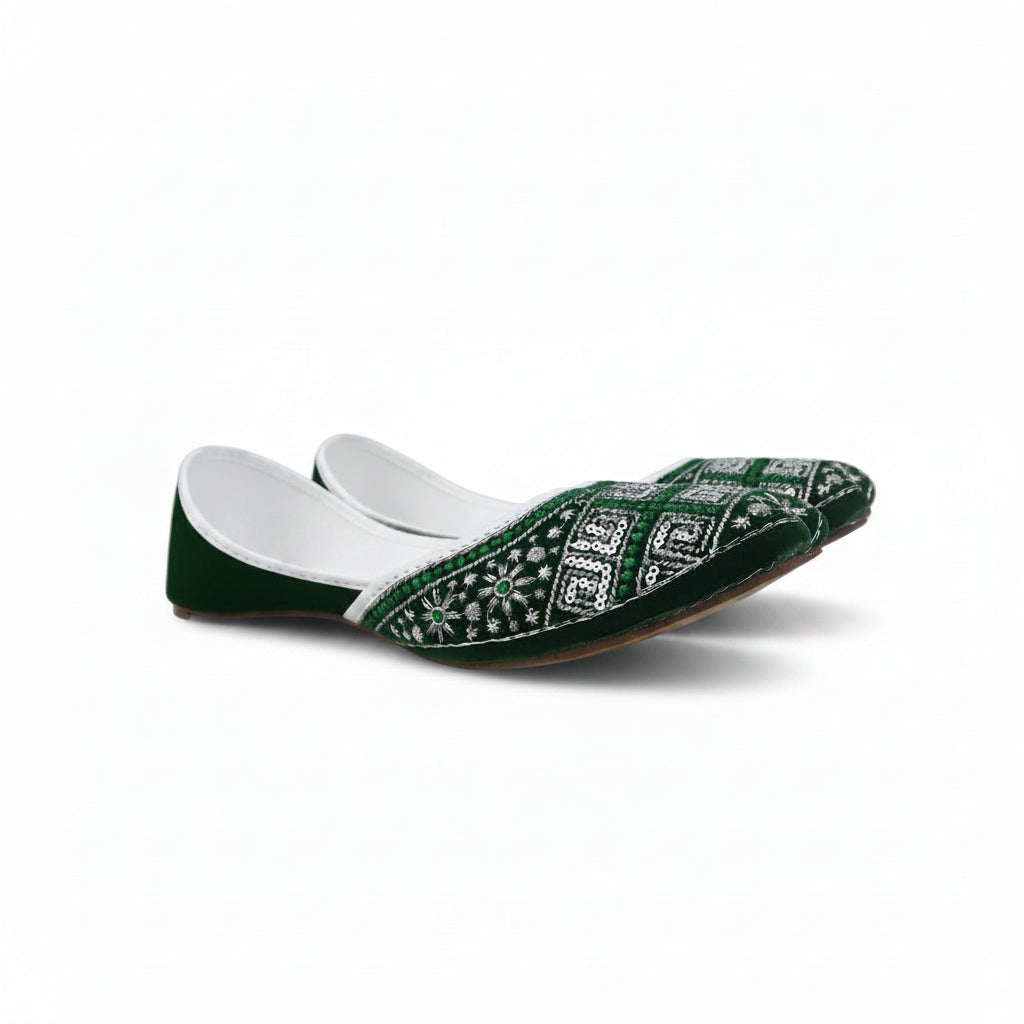 A single green velvet flat shoe with intricate white and silver embroidery on the toe, photographed on a light gray fabric background.