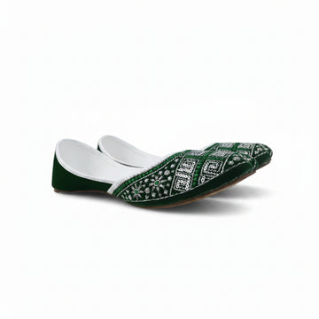 A single green velvet flat shoe with intricate white and silver embroidery on the toe, photographed on a light gray fabric background.