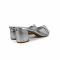 A pair of women's silver metallic block-heel mules with rhinestone-embellished straps, shown on a light gray background.