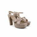 A pair of beige platform high-heeled sandals with criss-cross front straps and ankle straps, photographed on a light gray studio background.
