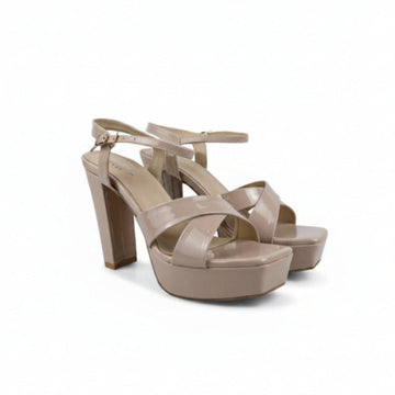 A pair of beige platform high-heeled sandals with criss-cross front straps and ankle straps, photographed on a light gray studio background.