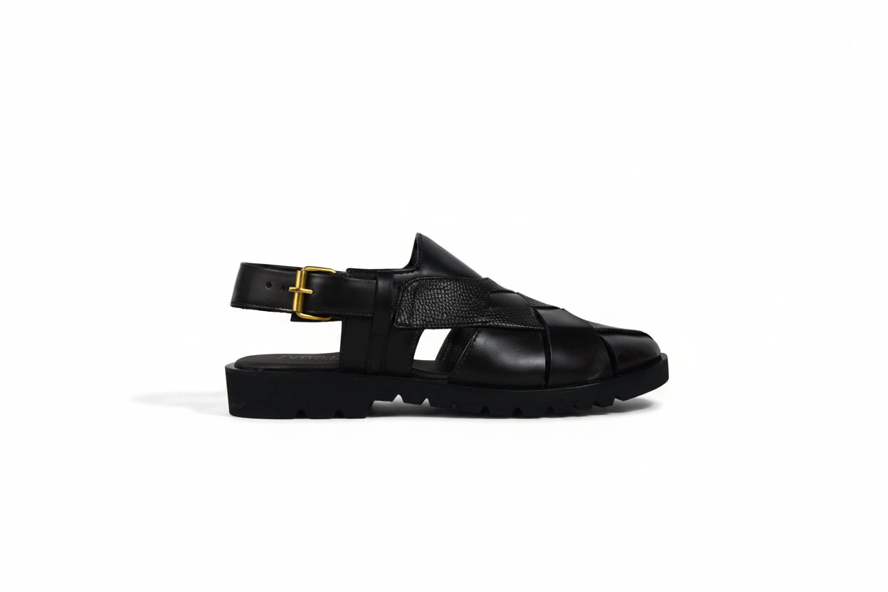 A single black leather sandal with a chunky platform sole, cutout straps, and a black ankle strap with a gold buckle, shown in profile against a light gray background.