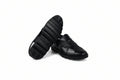 A pair of black leather men's loafers, with one shoe standing upright to show the textured sole and the other lying flat to display the woven strap pattern, set against a white studio backdrop.