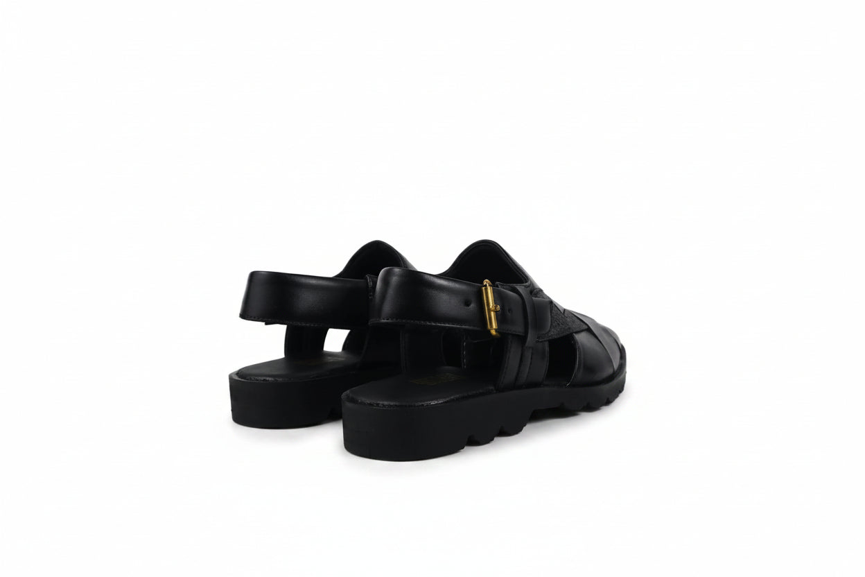 A pair of black leather platform sandals with cutout straps and a small gold buckle detail, photographed on a light gray studio background.
