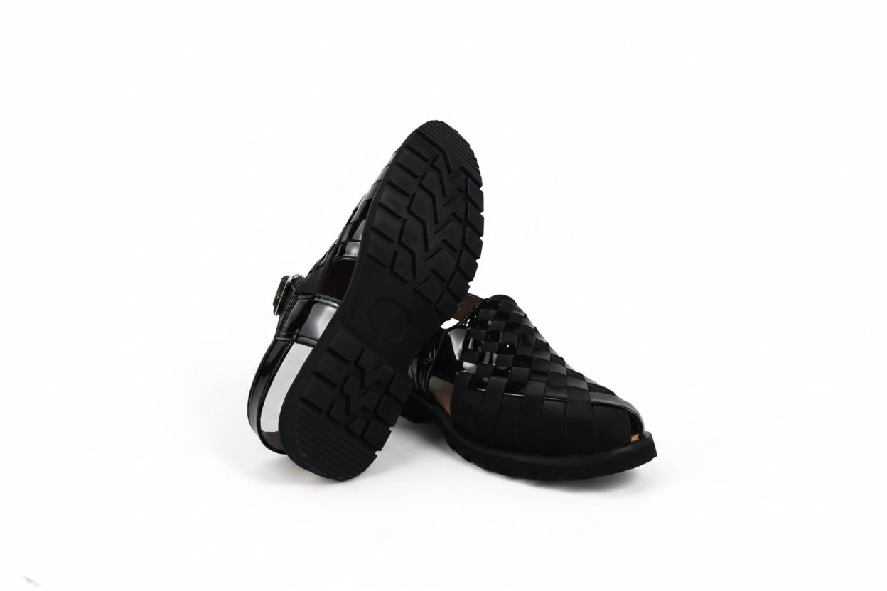 A pair of black leather woven sandals with a chunky lug sole, shown on a white studio background.